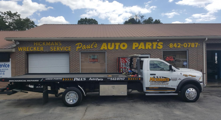 A flatbed tow truck parked in front of Paul's Auto Parts building.