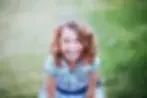 Blurred person in a blue shirt standing outdoors against a green background
