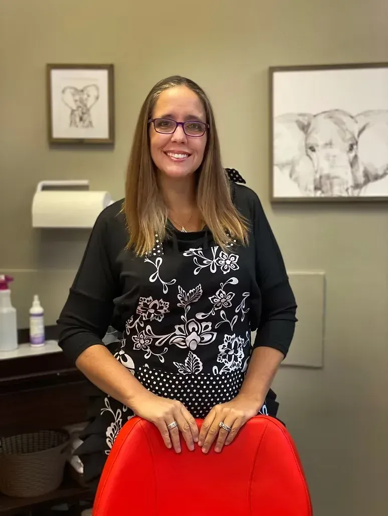 Woman smiling in an office, seated behind a red chair with framed cow artwork on the wall.
