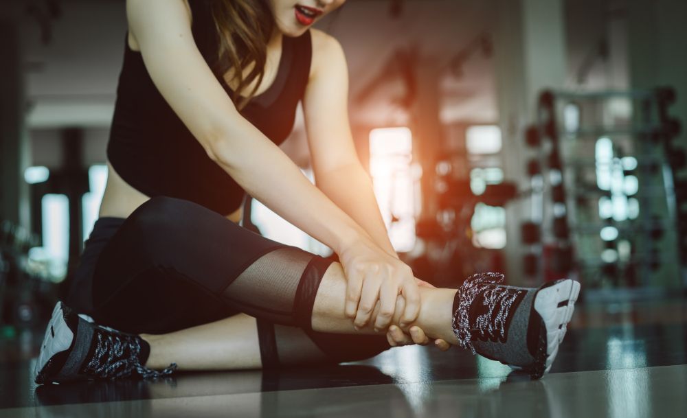 A Person in Gym Clothes Sits on the Floor Holding Their Ankle in Pain — Elevate Injury Management in Sandy Bay, TAS