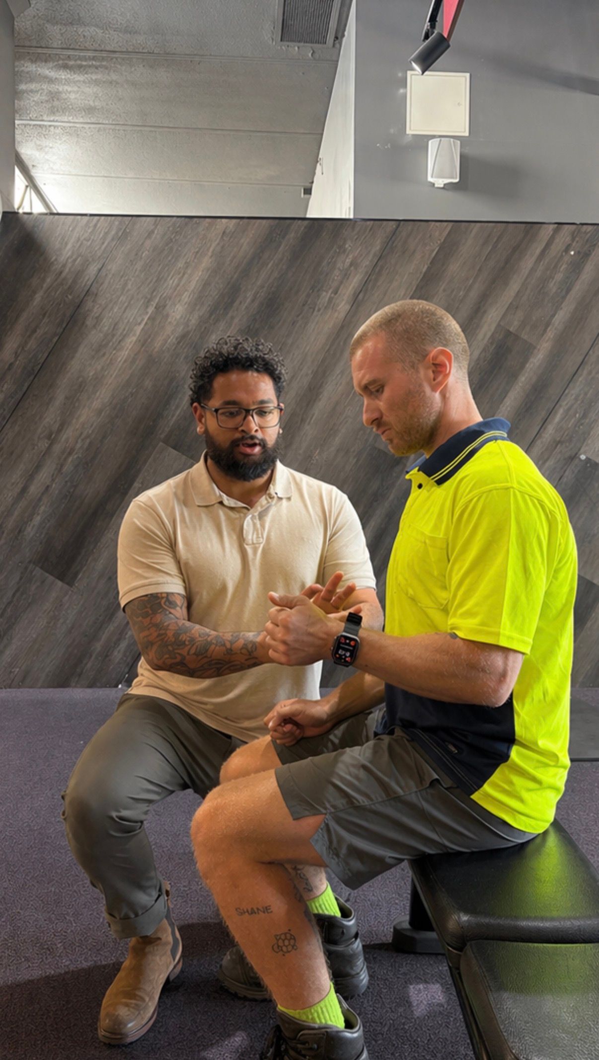 Two people seated indoors, one demonstrating a hand exercise on the other's wrist.— Elevate Injury Management in Sandy Bay, TAS