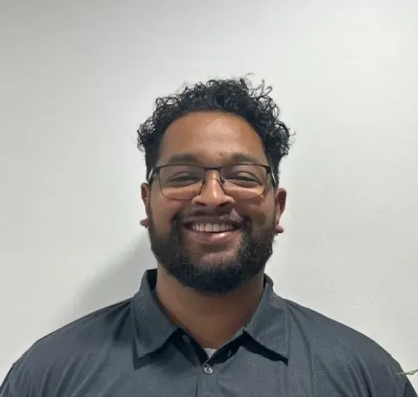Smiling person with glasses and beard in a dark grey shirt against a plain light background — Elevate Injury Management in Sandy Bay, TAS
