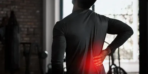 A Person Standing in a Gym, Holding Their Lower Back — Elevate Injury Management in Sandy Bay, TAS