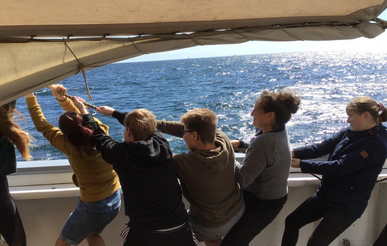 A group of people are pulling a sailboat in the ocean