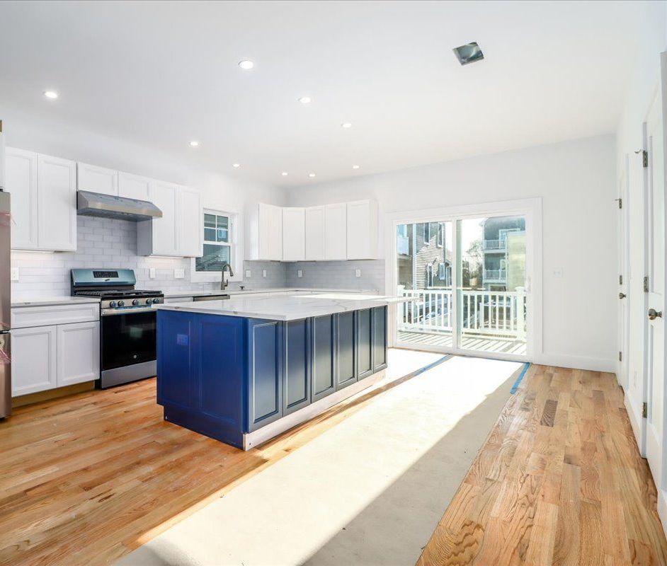 Modern kitchen with white cabinets, blue island, and light wood floors.