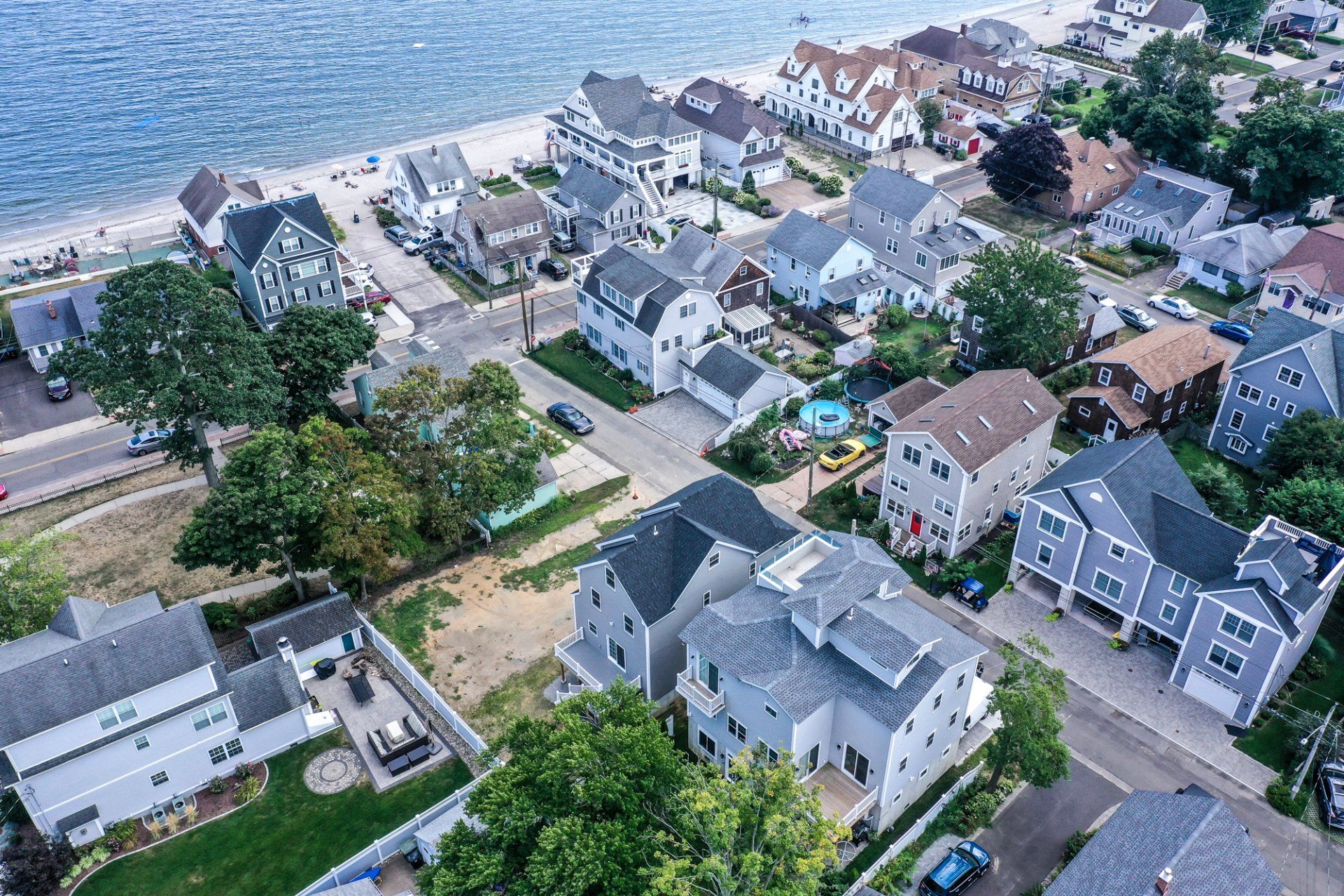 Aerial view of beachside houses, light blue water, and green trees.