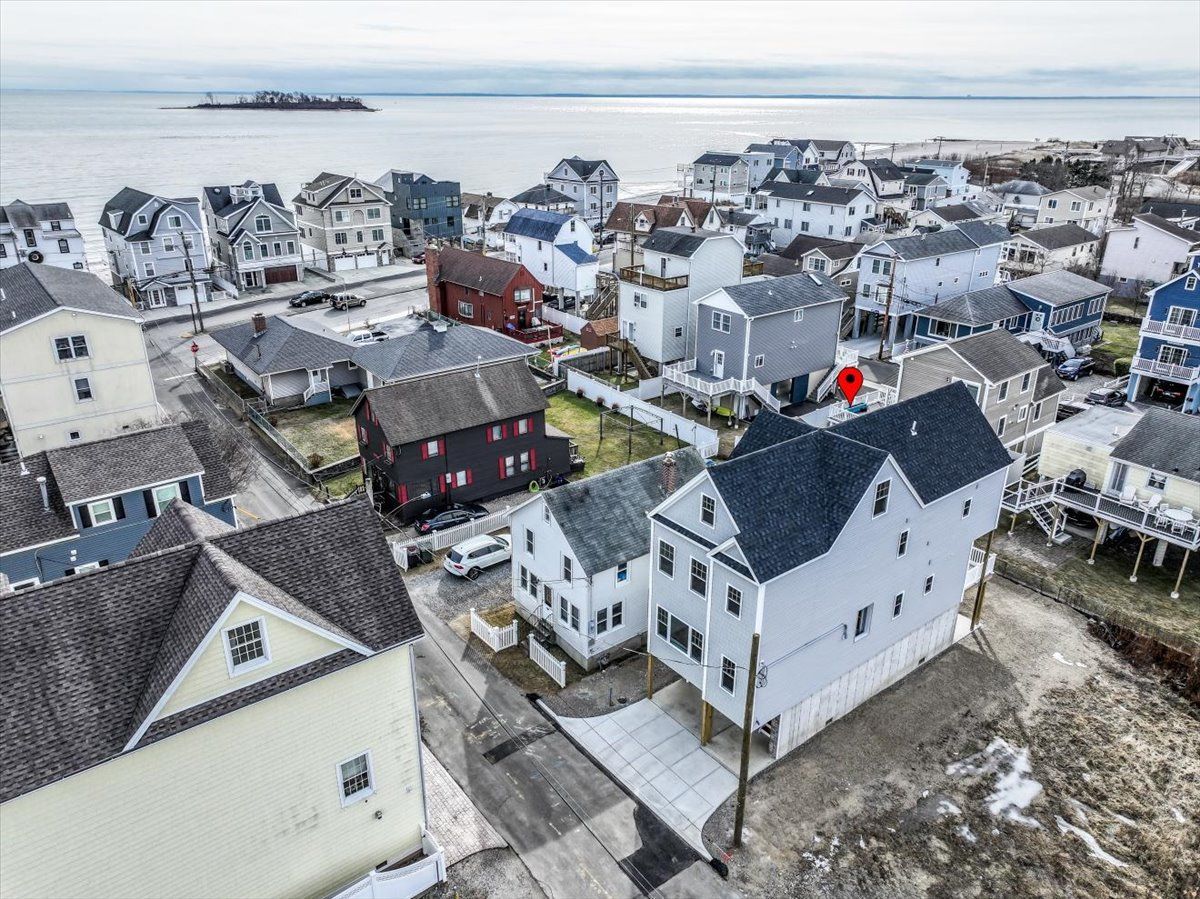 Aerial view of a coastal neighborhood with houses, a beach, and the ocean in the background.