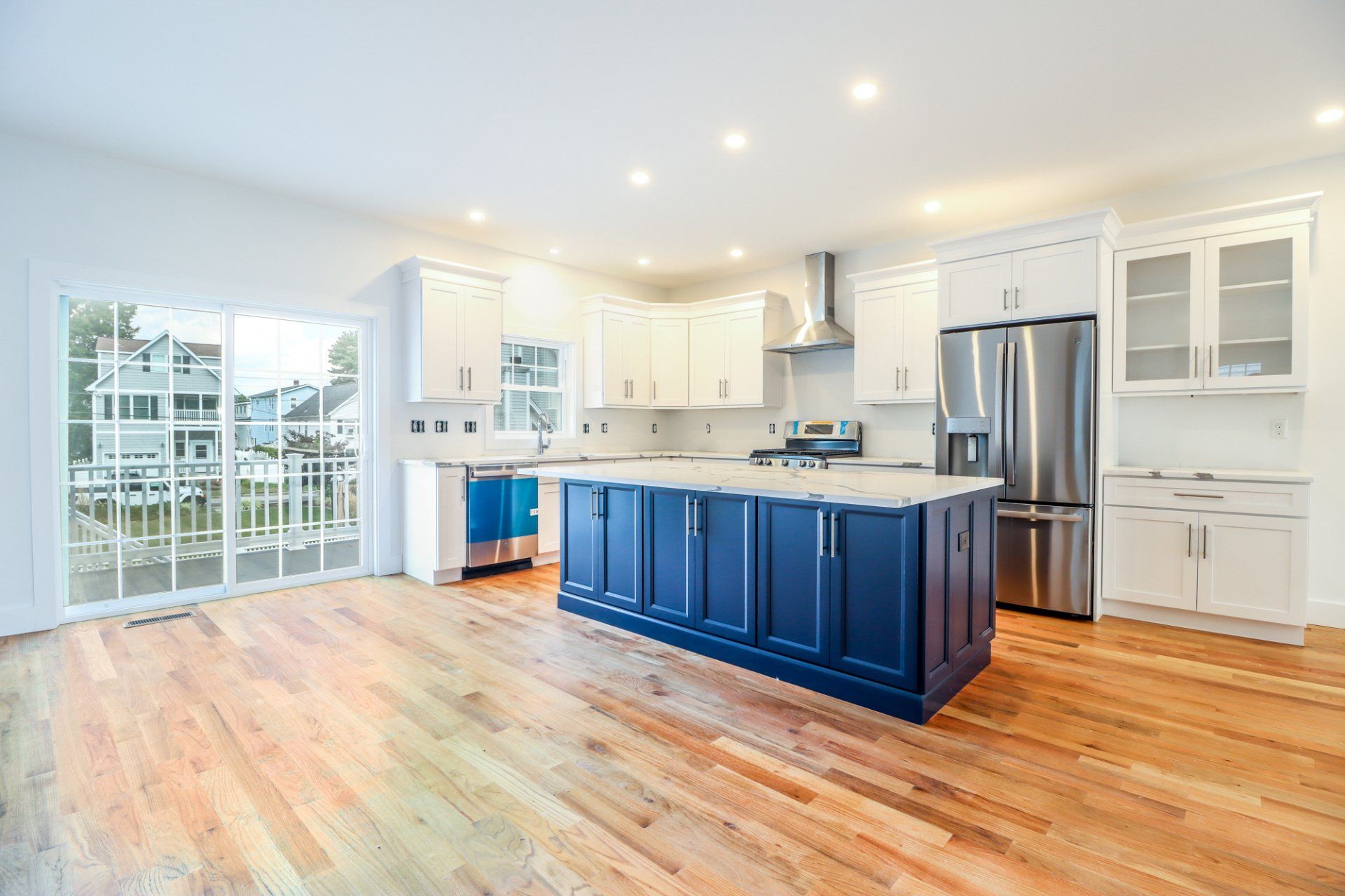 Modern kitchen with blue island, white cabinets, stainless steel appliances, and wooden floors.