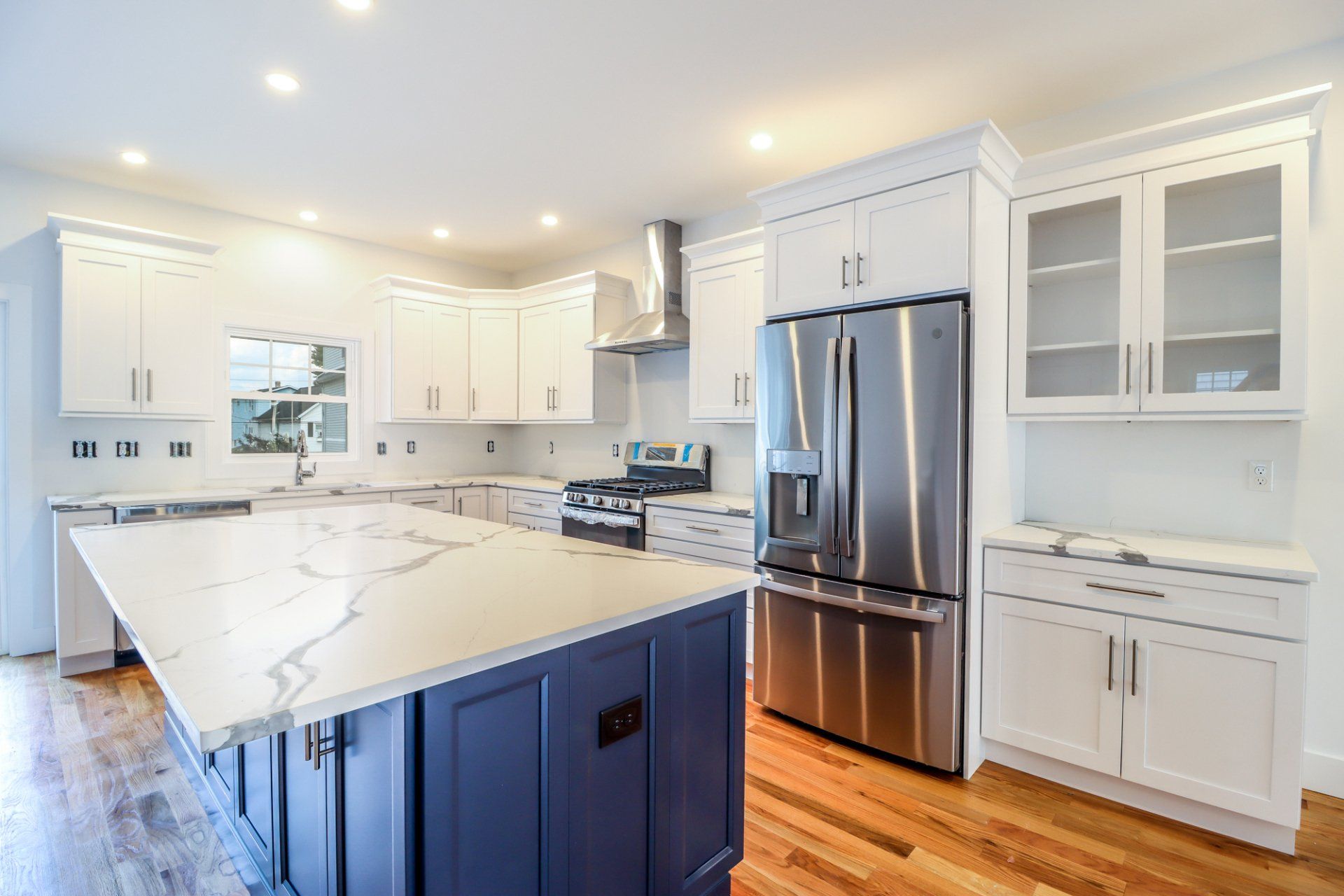 Modern kitchen with white cabinets, blue island, stainless steel refrigerator, and hardwood floors.