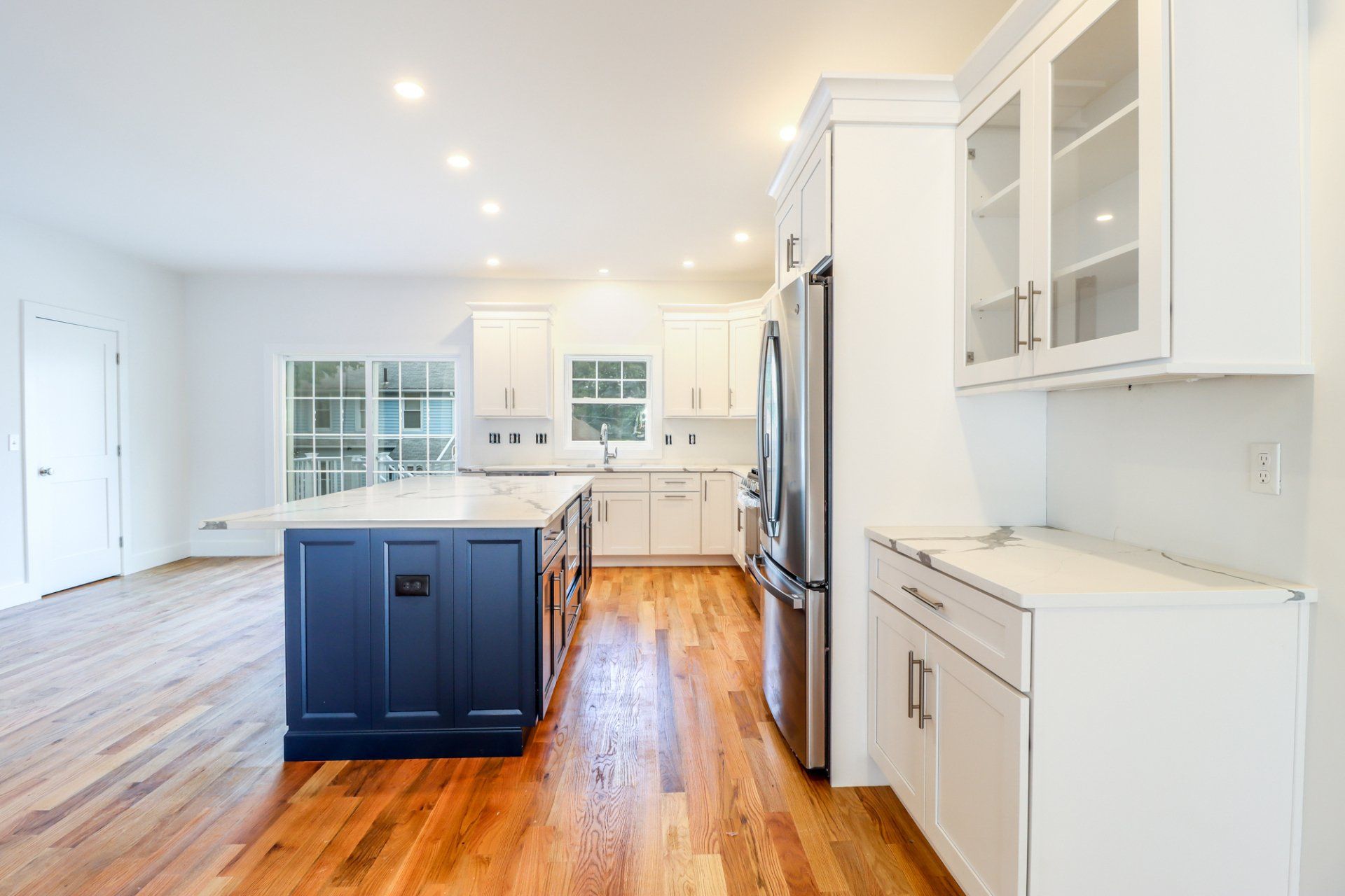 Bright white kitchen with navy island, stainless steel appliances, and hardwood floors.