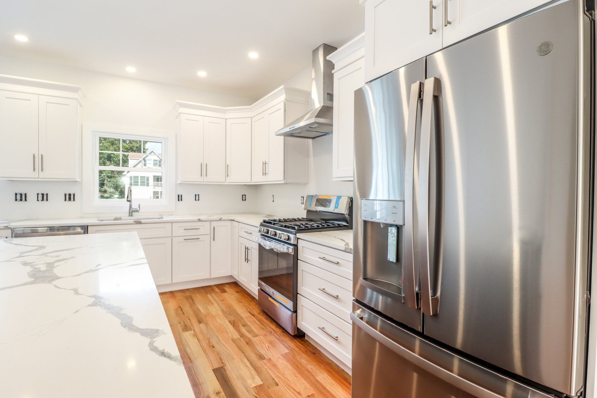 Bright white kitchen with stainless steel appliances and wood flooring.