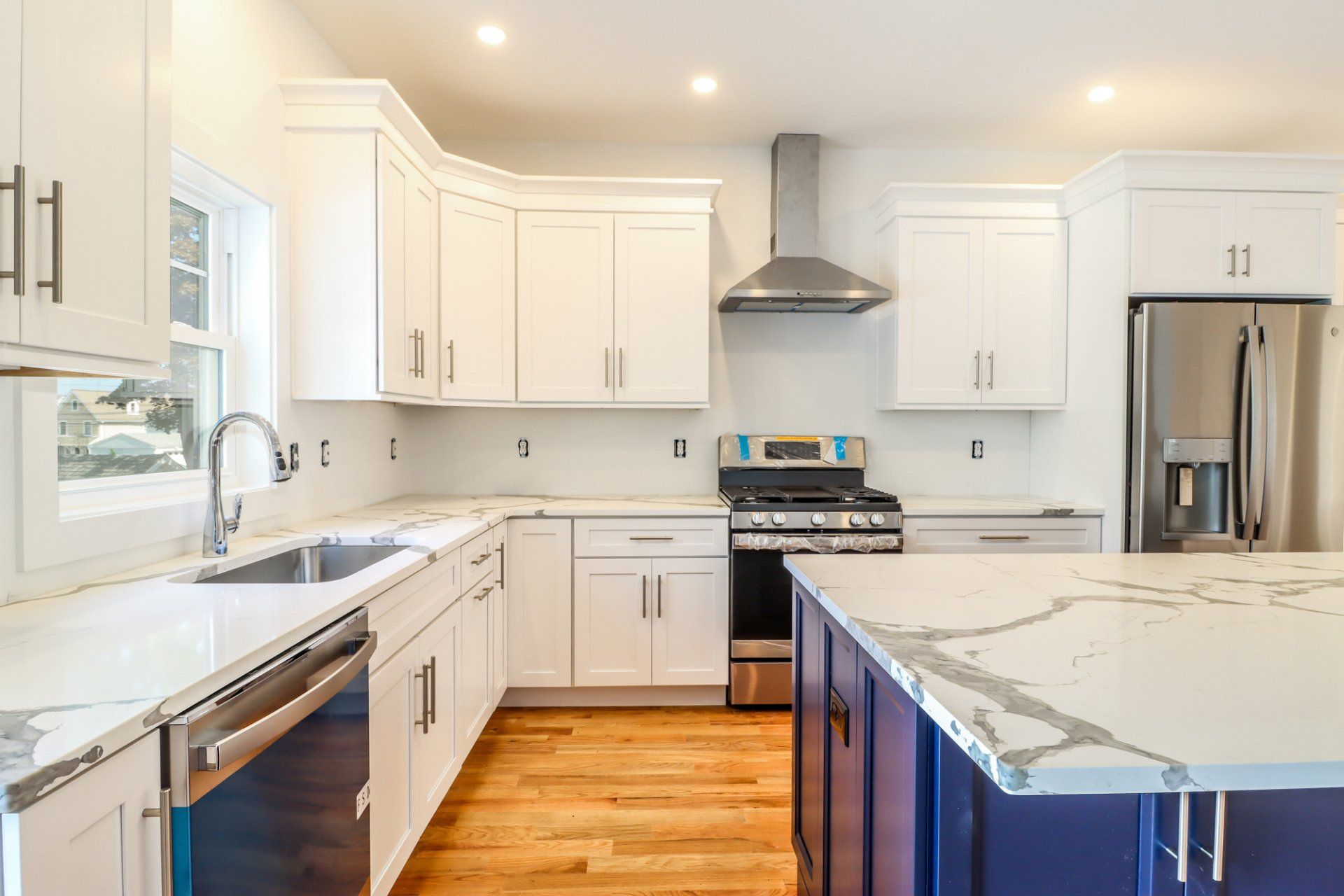Modern kitchen with white cabinets, stainless steel appliances, and a blue island with a marble countertop.