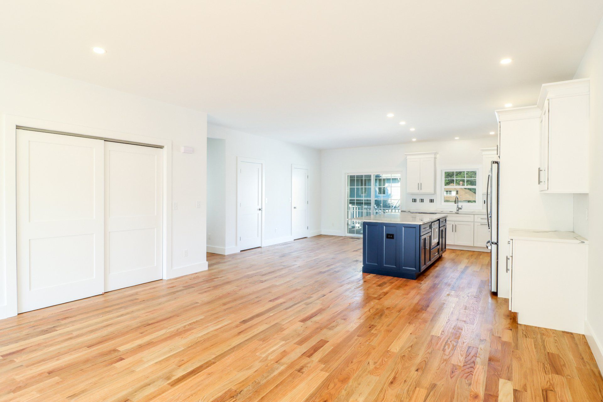 Open-concept kitchen and living area with hardwood floors, white walls, and a blue island.