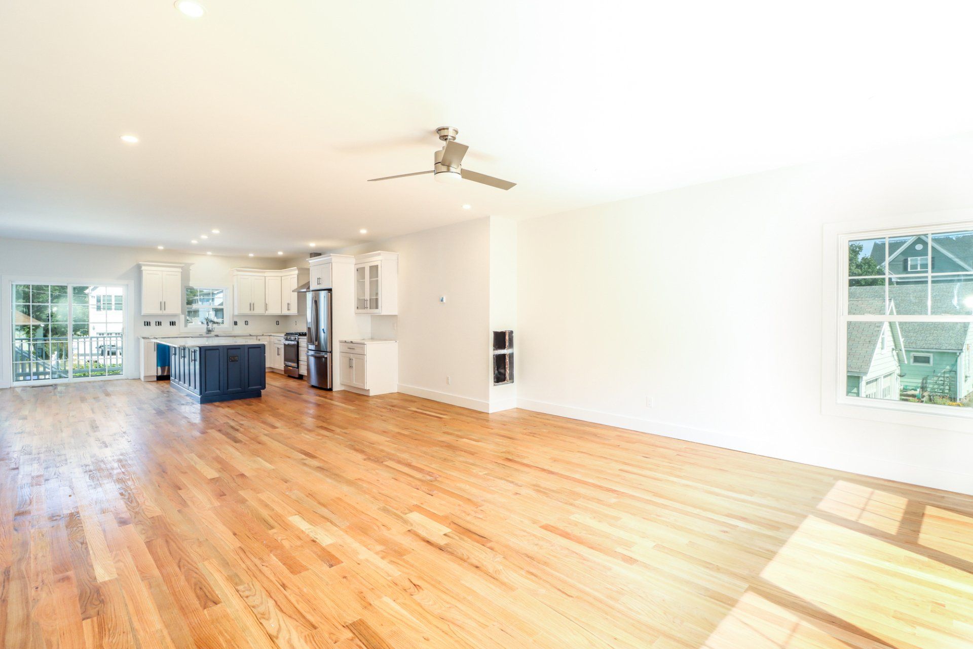 Bright, empty, open-concept living space with hardwood floors, white walls, and a blue kitchen island.