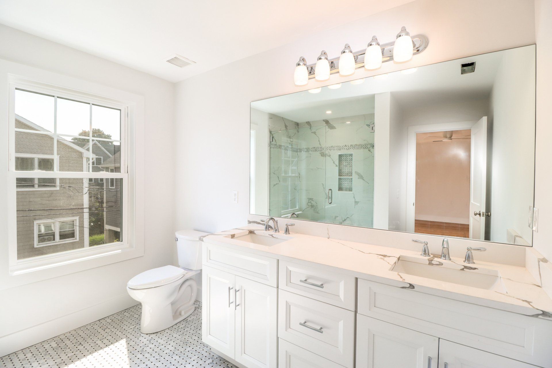 Bright, white bathroom with double vanity, large mirror, and glass shower.