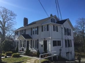 White two-story house with black shutters, chimney, and front door under a bright blue sky.