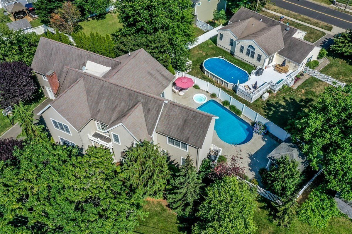 Aerial view of two houses with swimming pools in a lush, green, residential area.