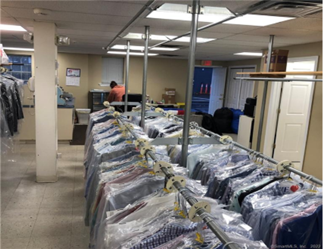 Dry cleaning shop with racks of clothes in plastic, a worker at a desk, fluorescent lights.