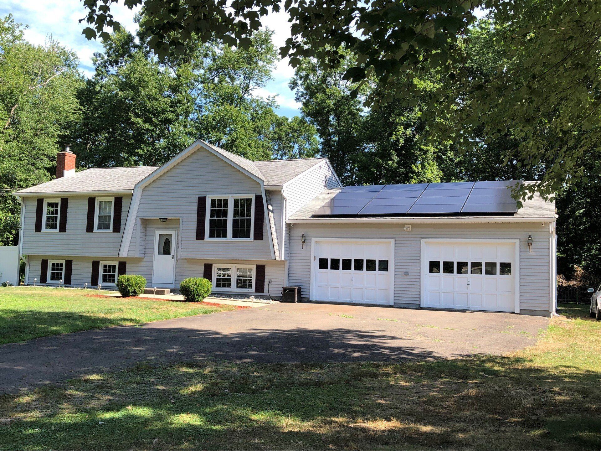 Light gray house with a two-car garage, solar panels on the roof, and a driveway.
