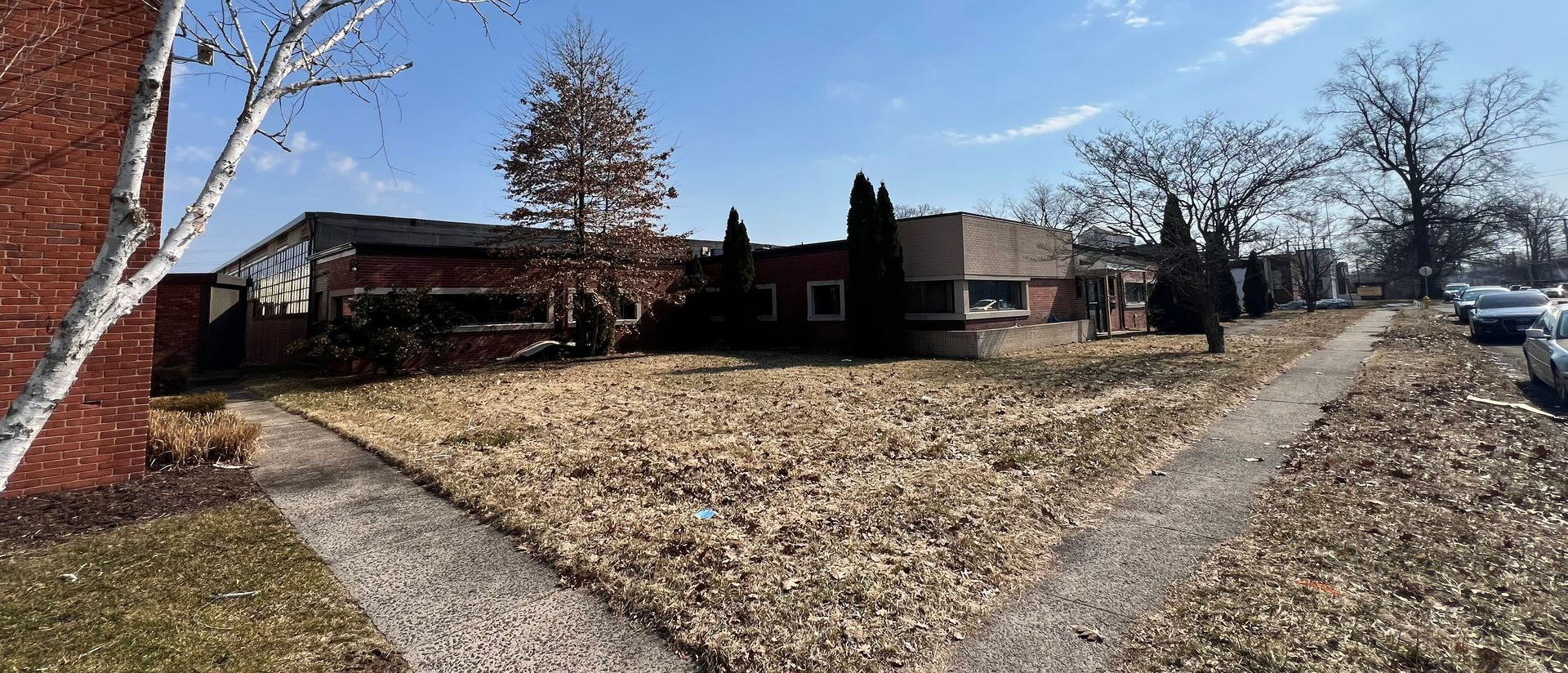 A brick building on a sunny day with a sidewalk covered in fallen leaves.