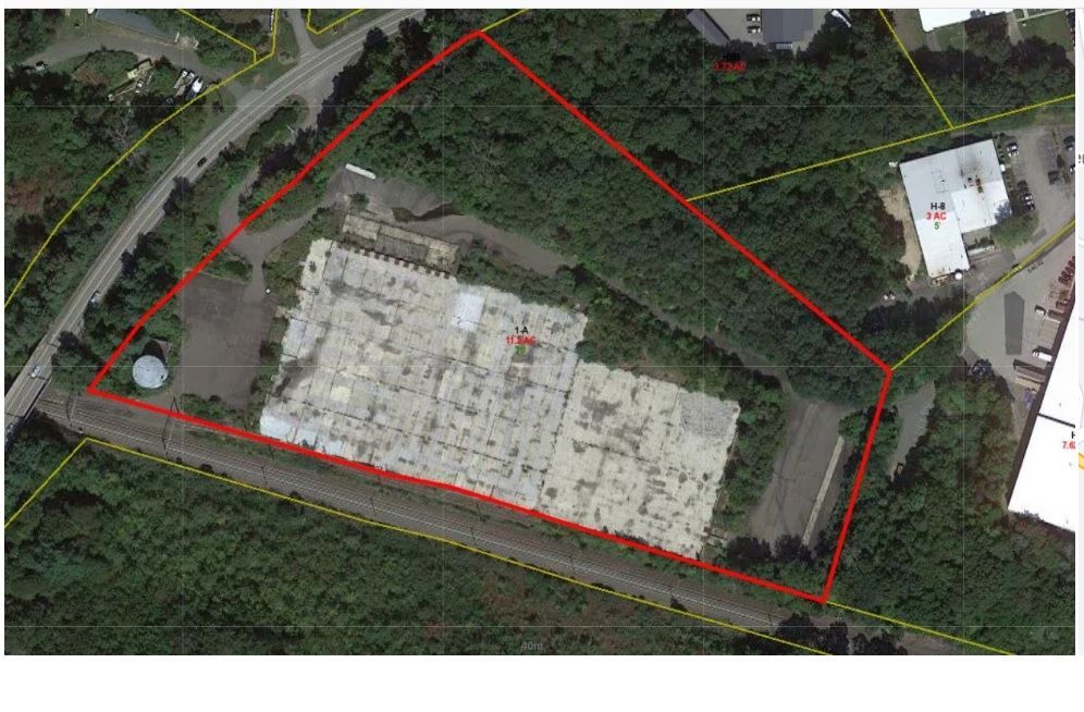 Aerial view of a commercial property outlined in red, showing a large building and surrounding vegetation.