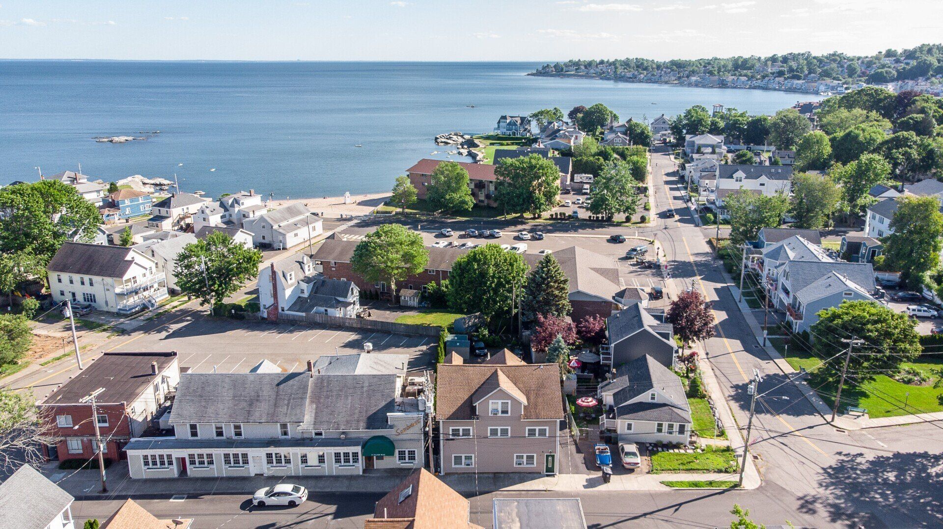 Coastal town aerial view with houses, beach, and water. Sunny day with blue sky.