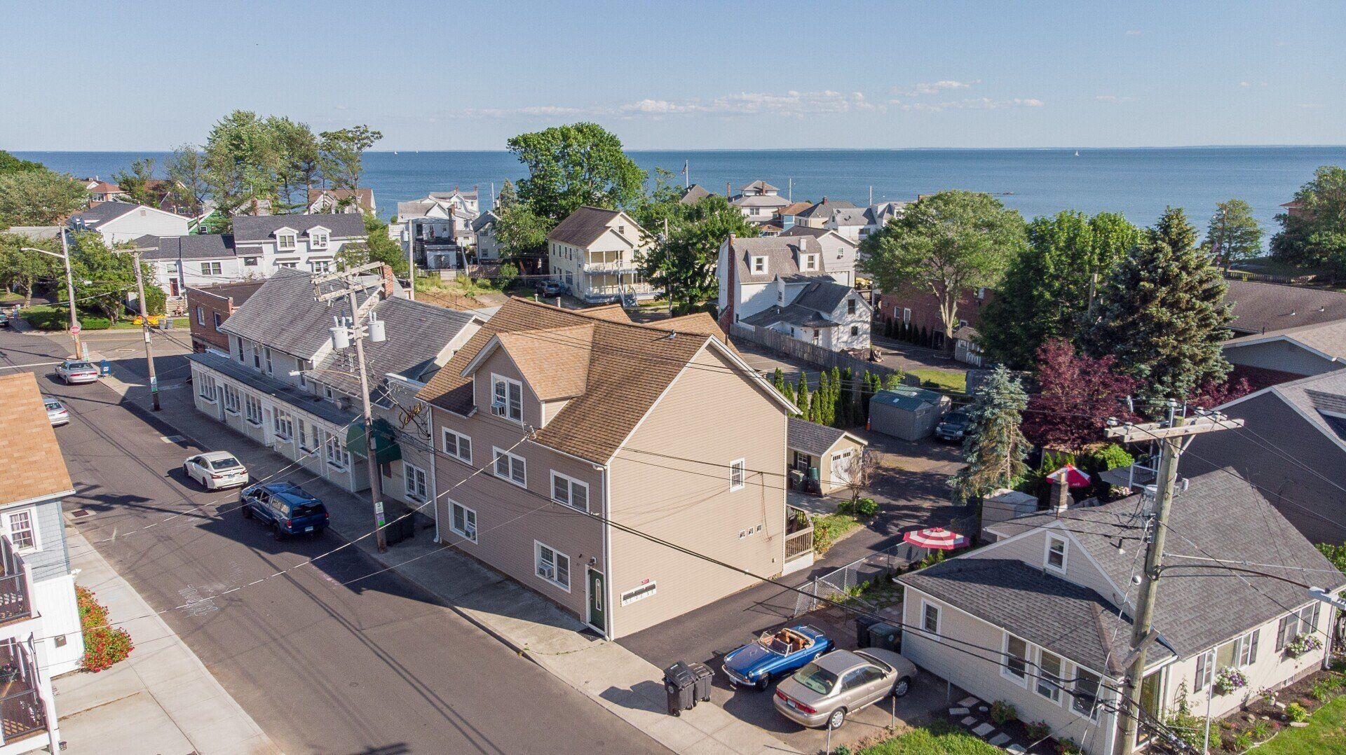 Street view of residential buildings with ocean in the background. Cars parked on the street. Sunny day.