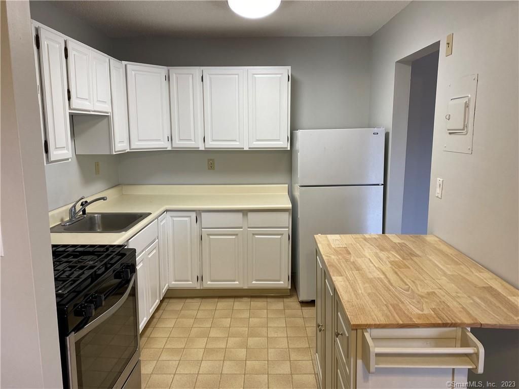 Small kitchen with white cabinets, appliances, and a butcher block island.
