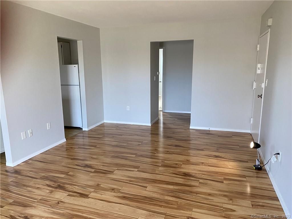 Empty room with wood-look floor, gray walls, and open doorways to kitchen and another room.