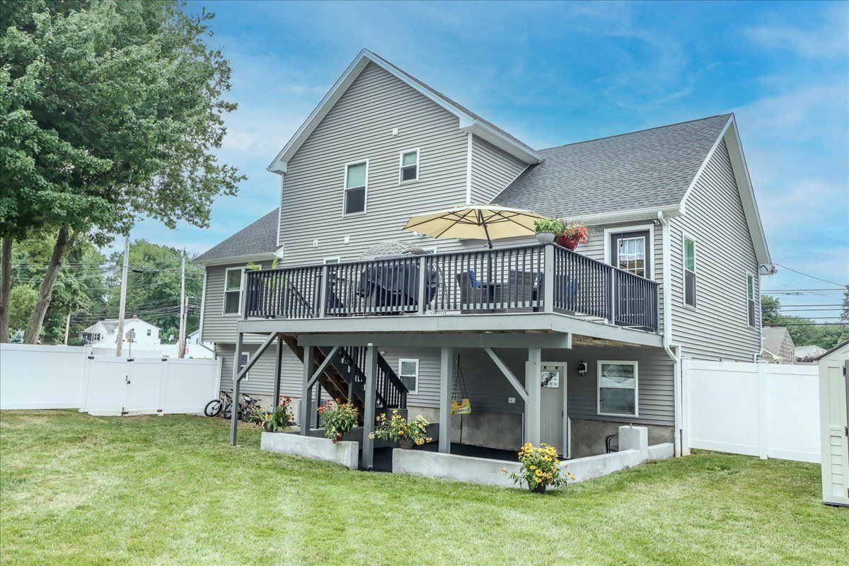 Gray house with a two-level deck, yellow umbrella, and green lawn against a blue sky.