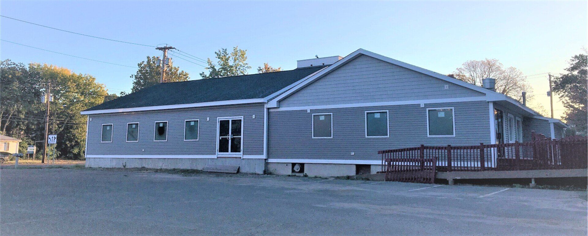 A gray building with a dark green roof and a wooden deck.