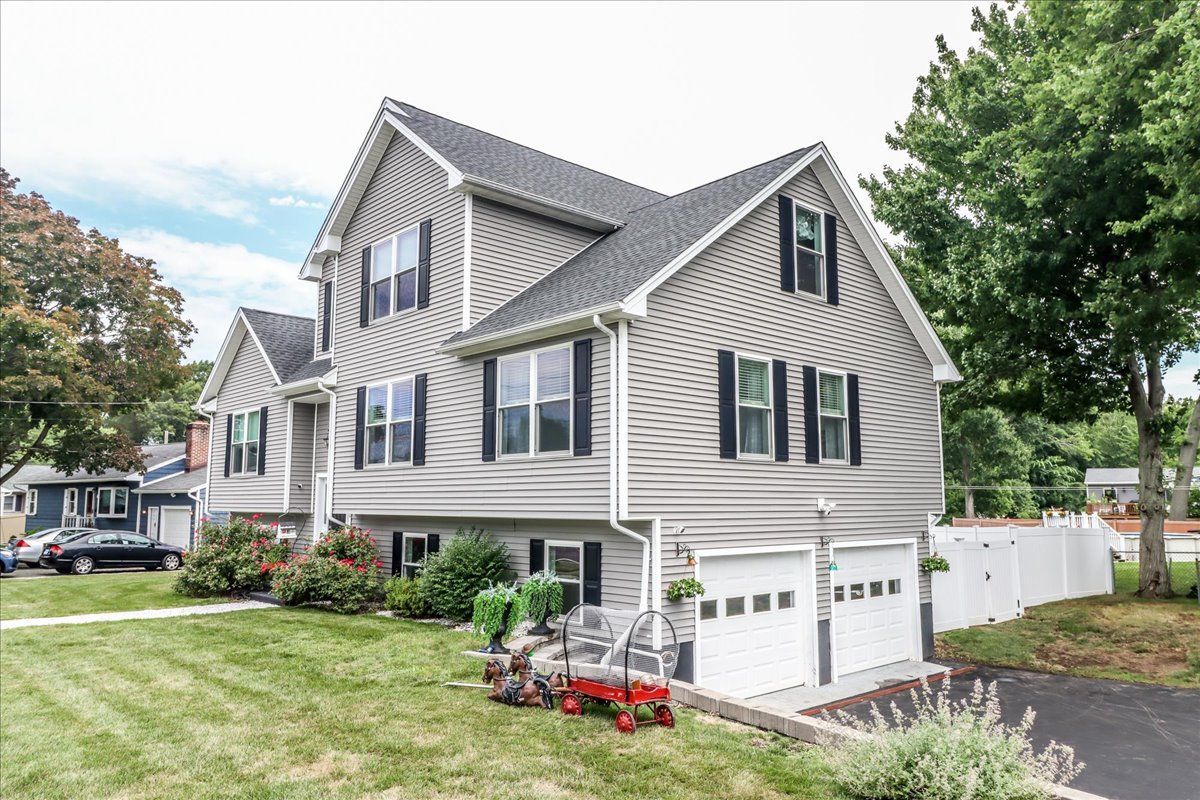 Two-story house with gray siding, black shutters, white garage door, and green lawn.