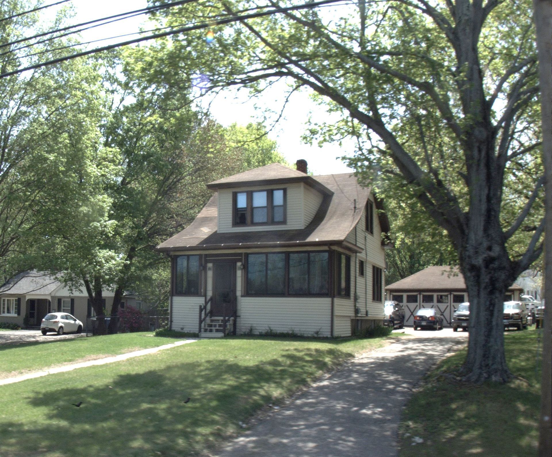 Tan two-story house with screened porch, driveway, and surrounding trees on a sunny day.
