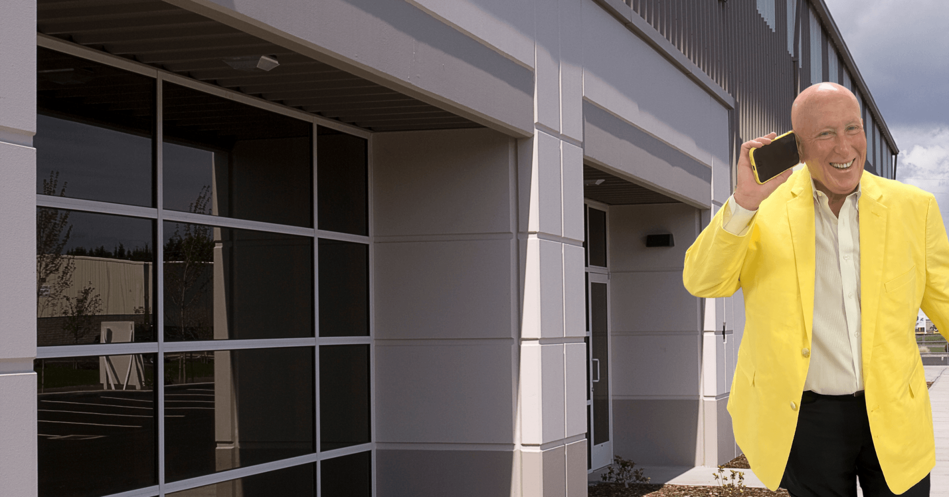 Man in yellow blazer on phone outside building with large windows.