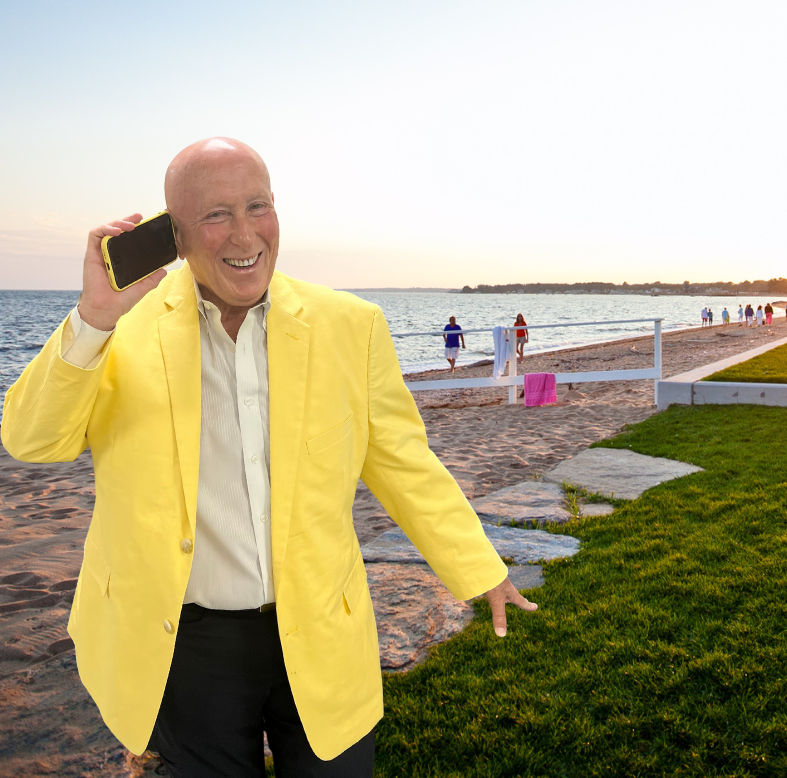 Man in yellow blazer on beach talking on phone.