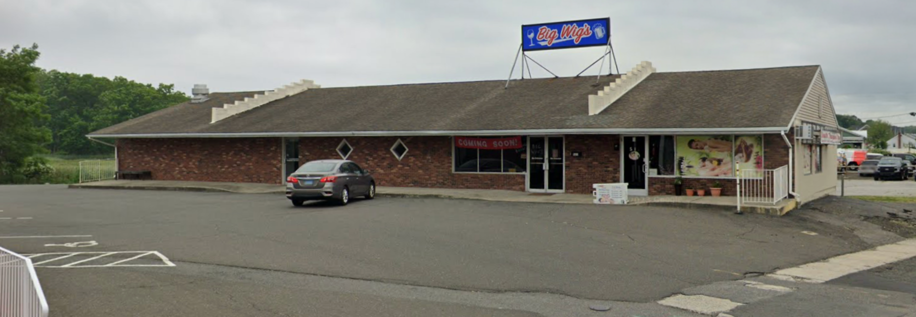 A one-story brick building with a sign on top, parking lot, and a car parked in front.