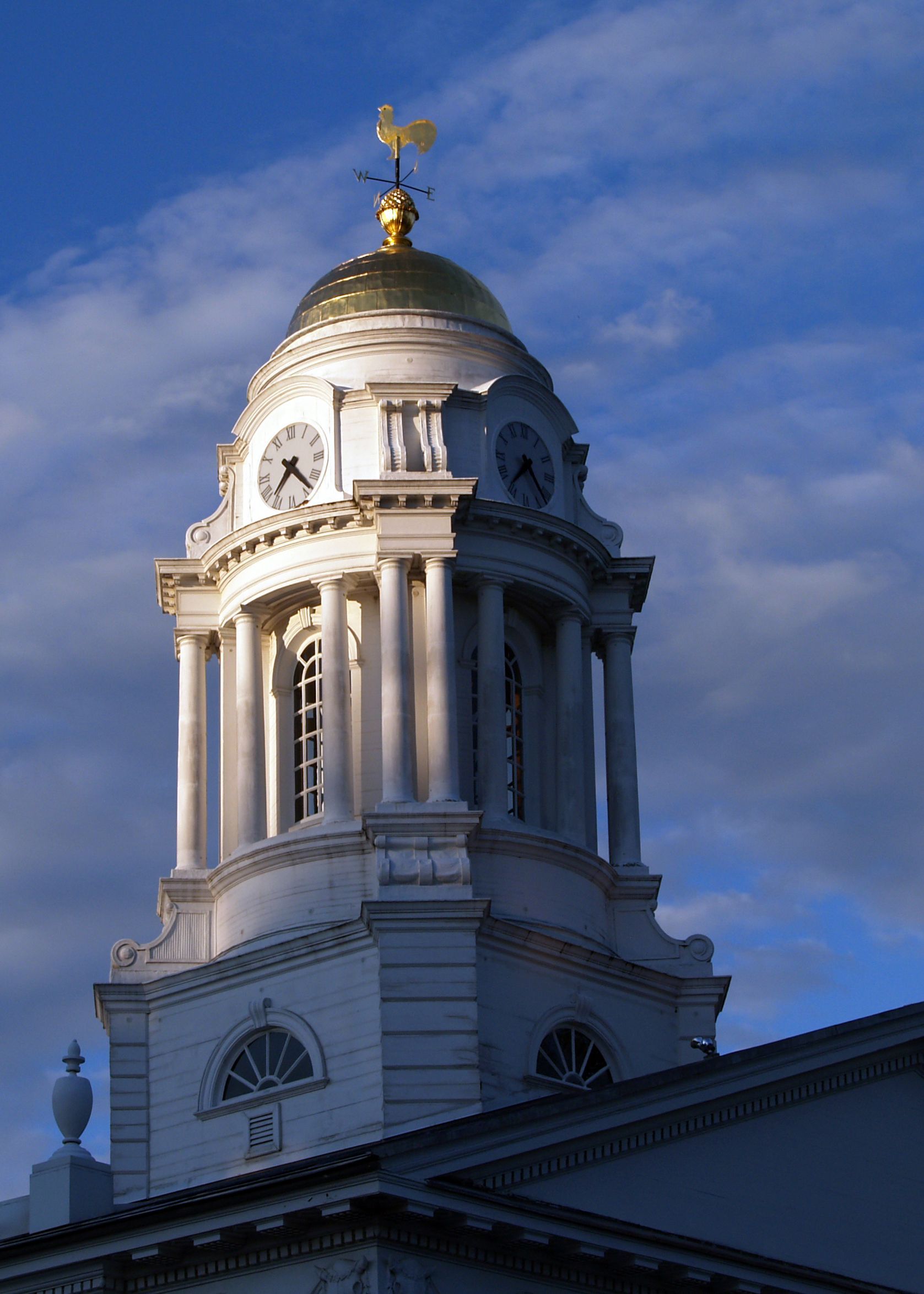 White domed building with clock tower, golden dome top, blue sky backdrop.