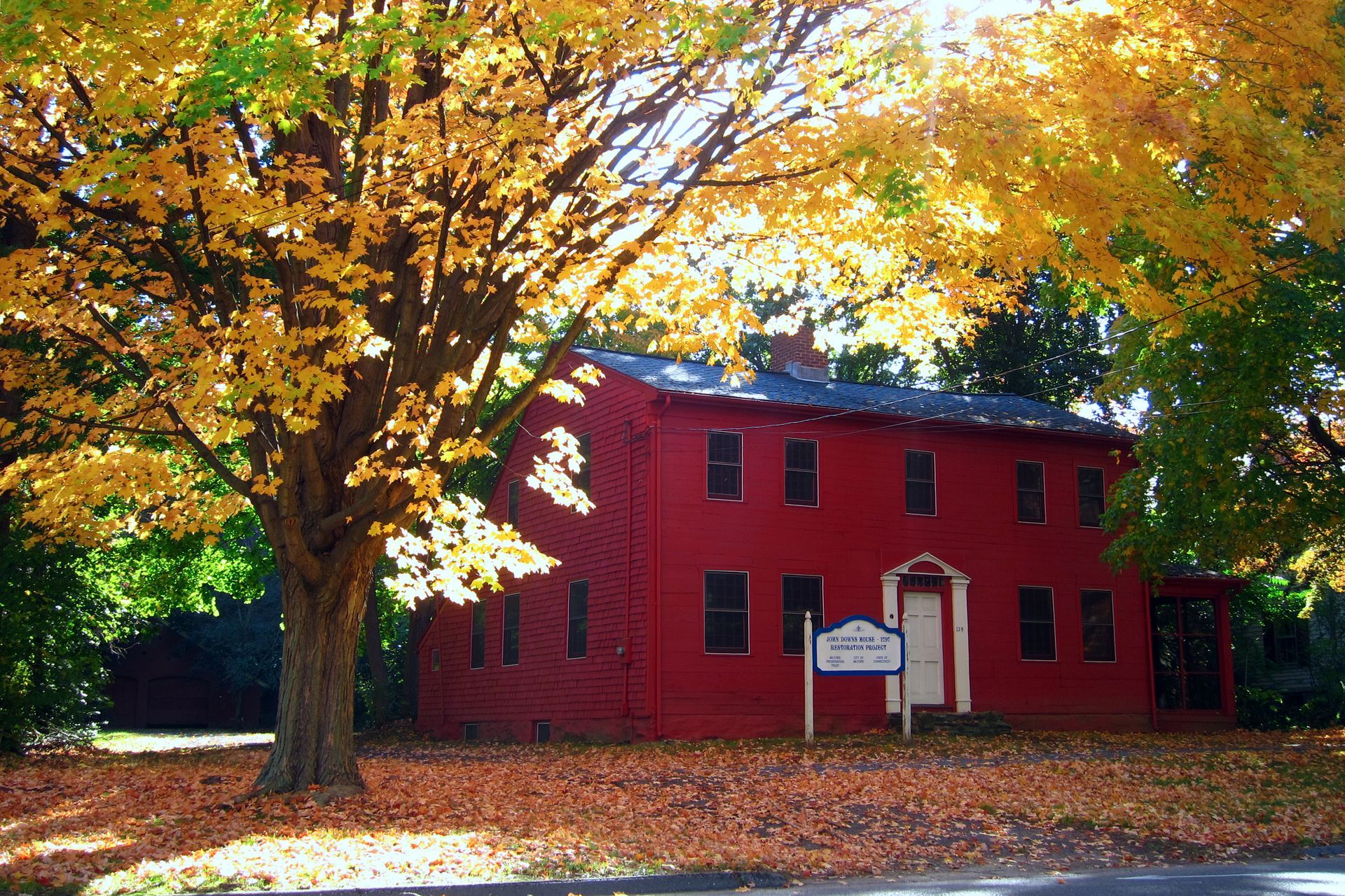Red house with yellow autumn trees. Sign in front.