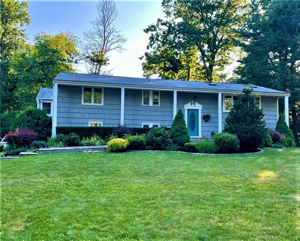 Gray ranch-style house with blue door and lush green lawn and landscaping.