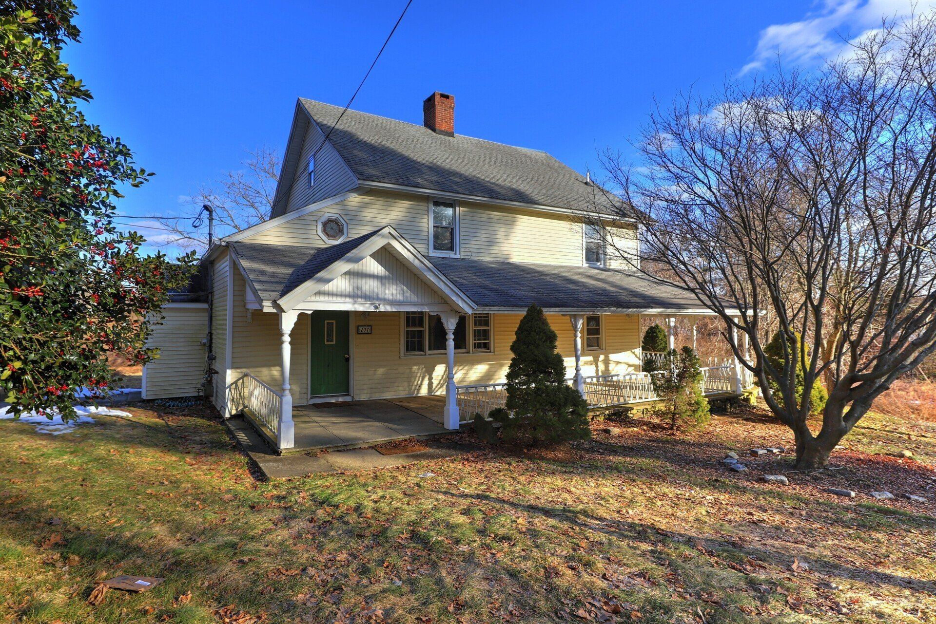 Two-story yellow house with porch and chimney under blue sky.
