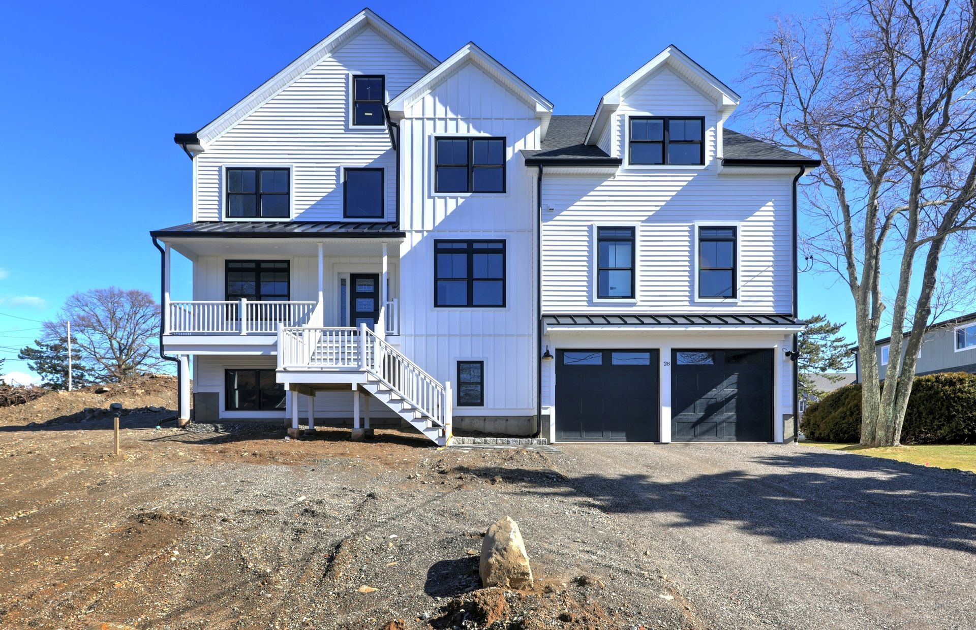 White, modern house with black trim, two-car garage, and porch; gravel yard; clear blue sky.