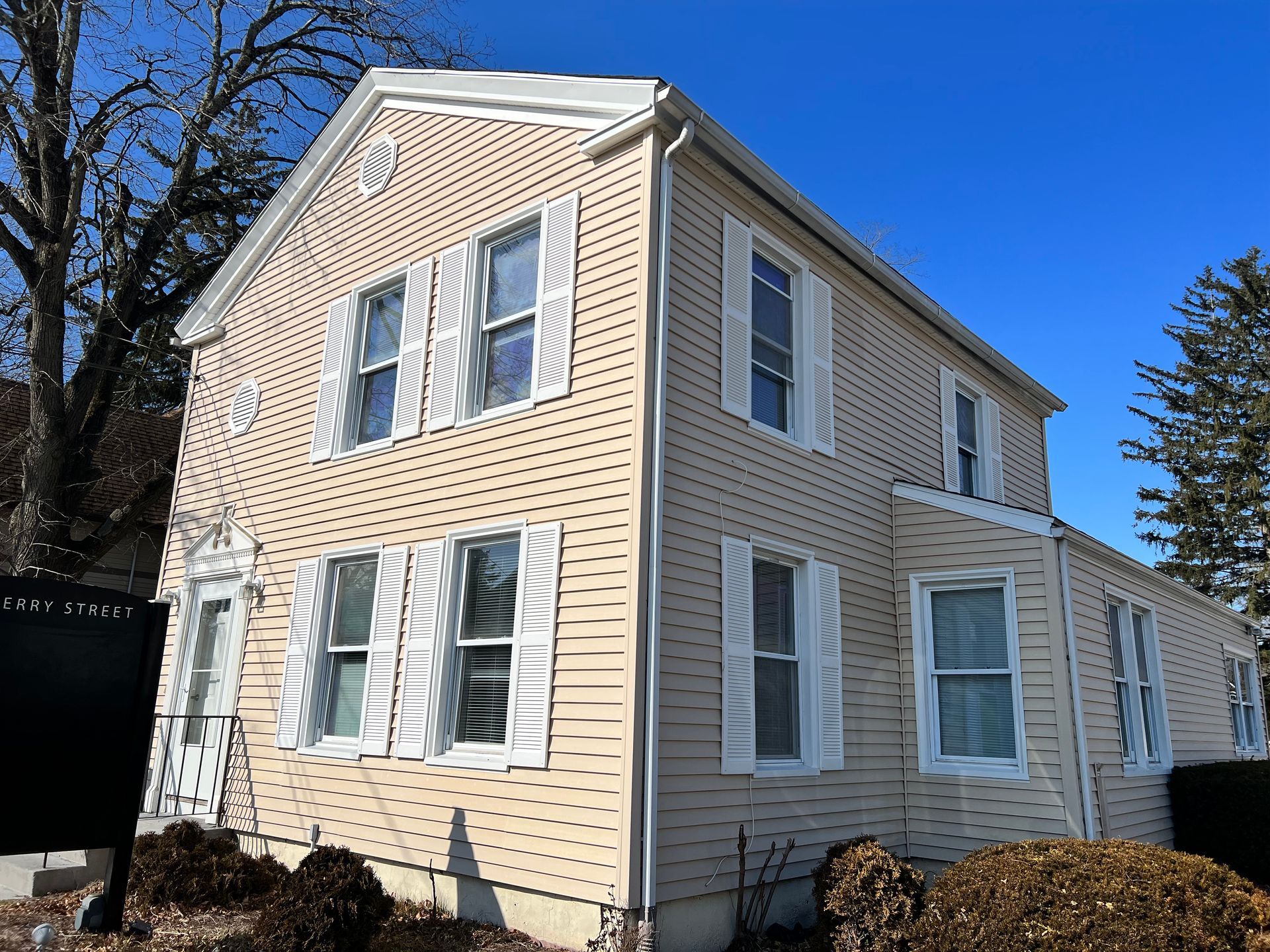 Two-story beige house with white shutters and a clear blue sky.