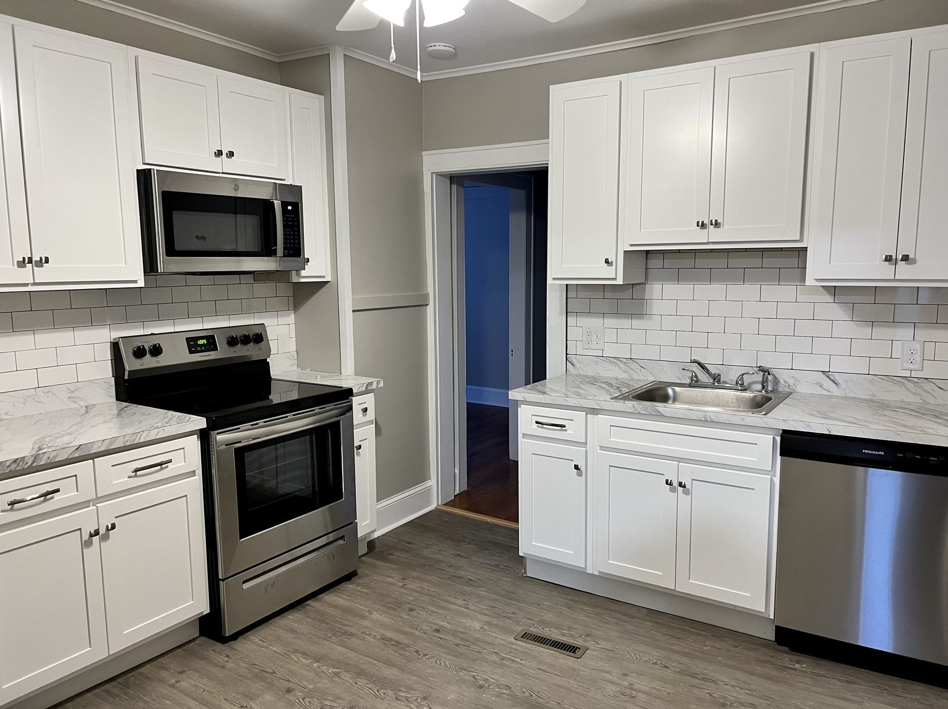 White kitchen with stainless steel appliances, grey countertops, and tile backsplash.