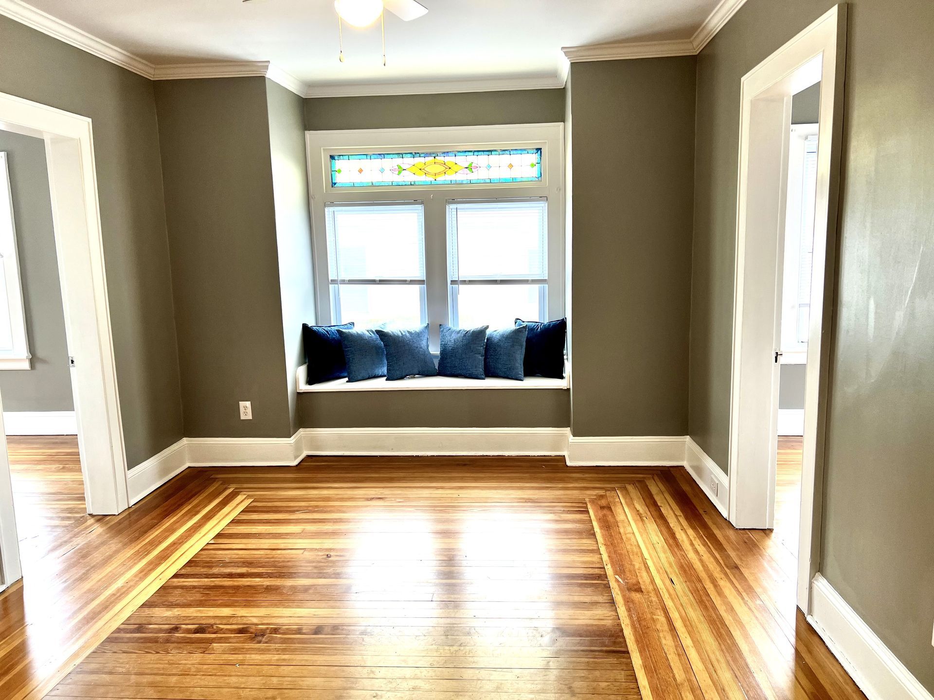 Empty room with hardwood floors, a bay window with blue cushions, and white trim.