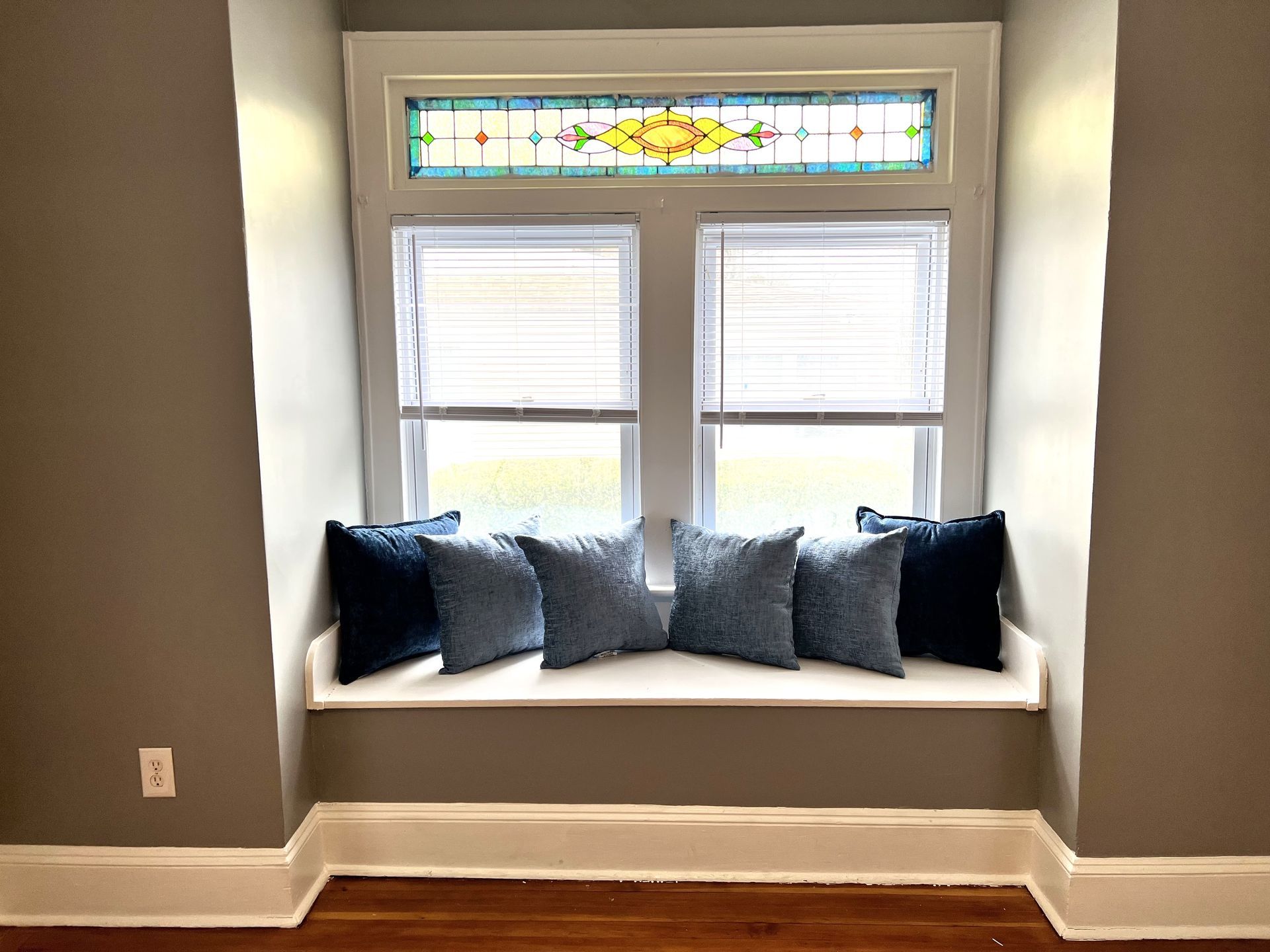 Window seat with gray walls, stained glass, and blue pillows.