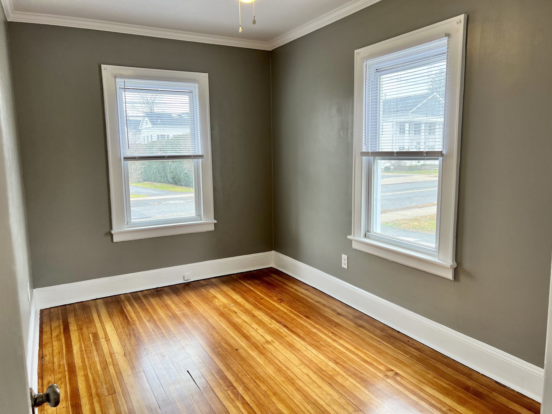 Empty room with two windows, painted gray walls, hardwood floor, white trim.