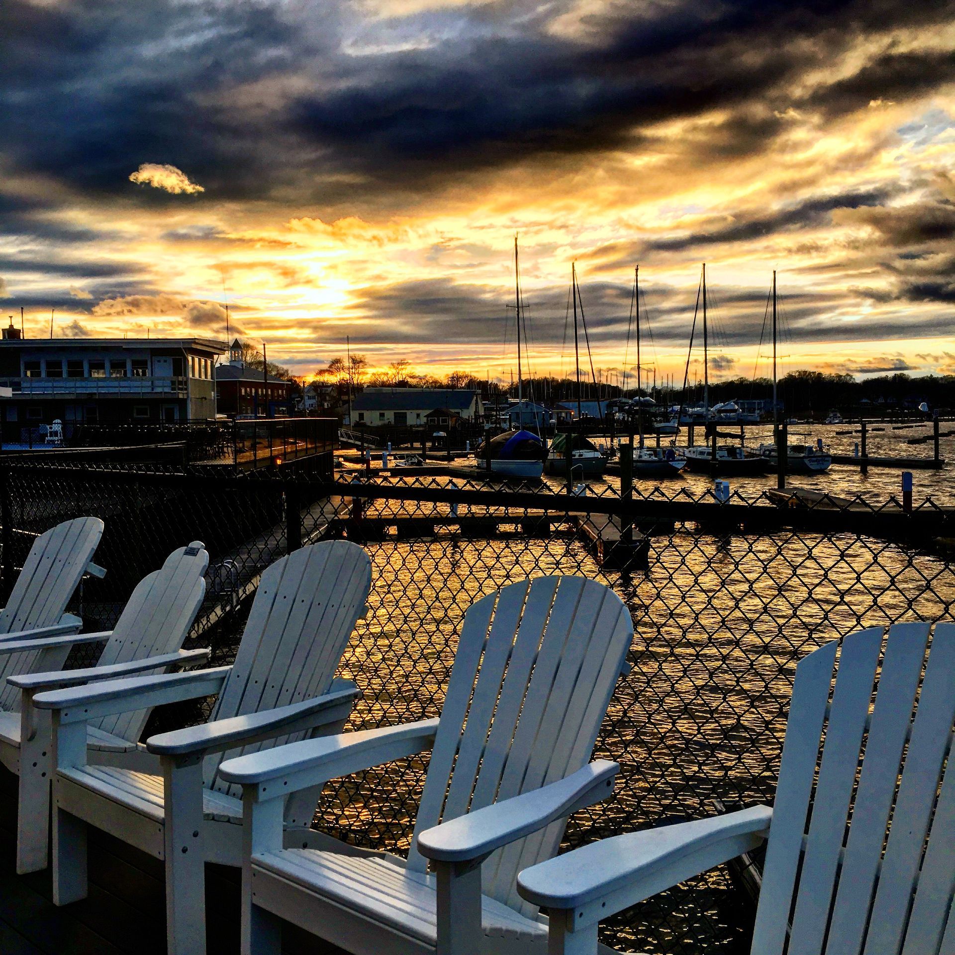 White Adirondack chairs overlooking a marina at sunset; golden light reflecting on the water.