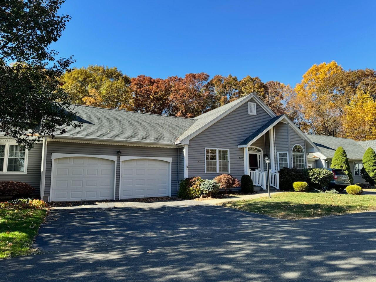 Gray house with two-car garage, front door, and fall foliage in the background under a blue sky.