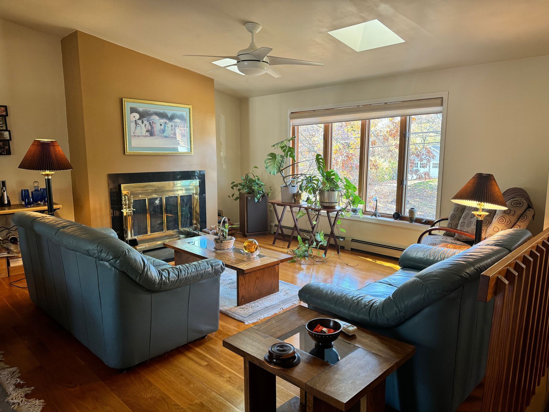 Living room with sofas, fireplace, large window, plants, and hardwood floors.
