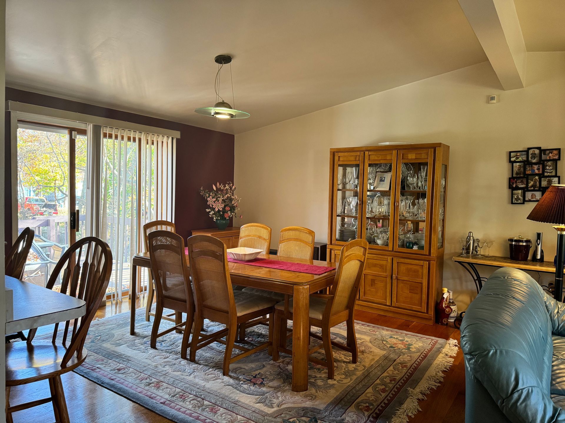 Dining room with wooden furniture, including a table, chairs, and a display cabinet, on a patterned rug.